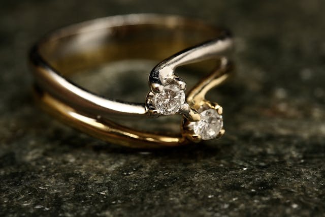 Anillo de compromiso de oro con dos diamantes engarzados sobre una superficie de piedra