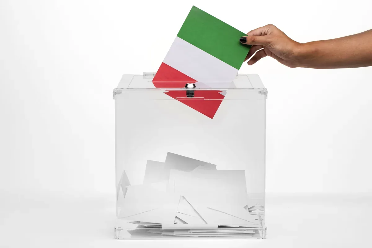 Mano que deposita una boleta verde, blanca y roja en una urna transparente
