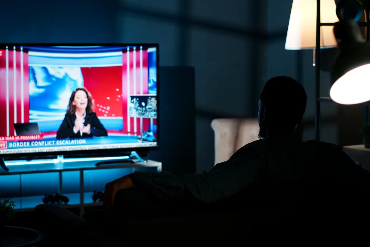 Persona que mira un noticiero en un televisor en una sala a oscuras