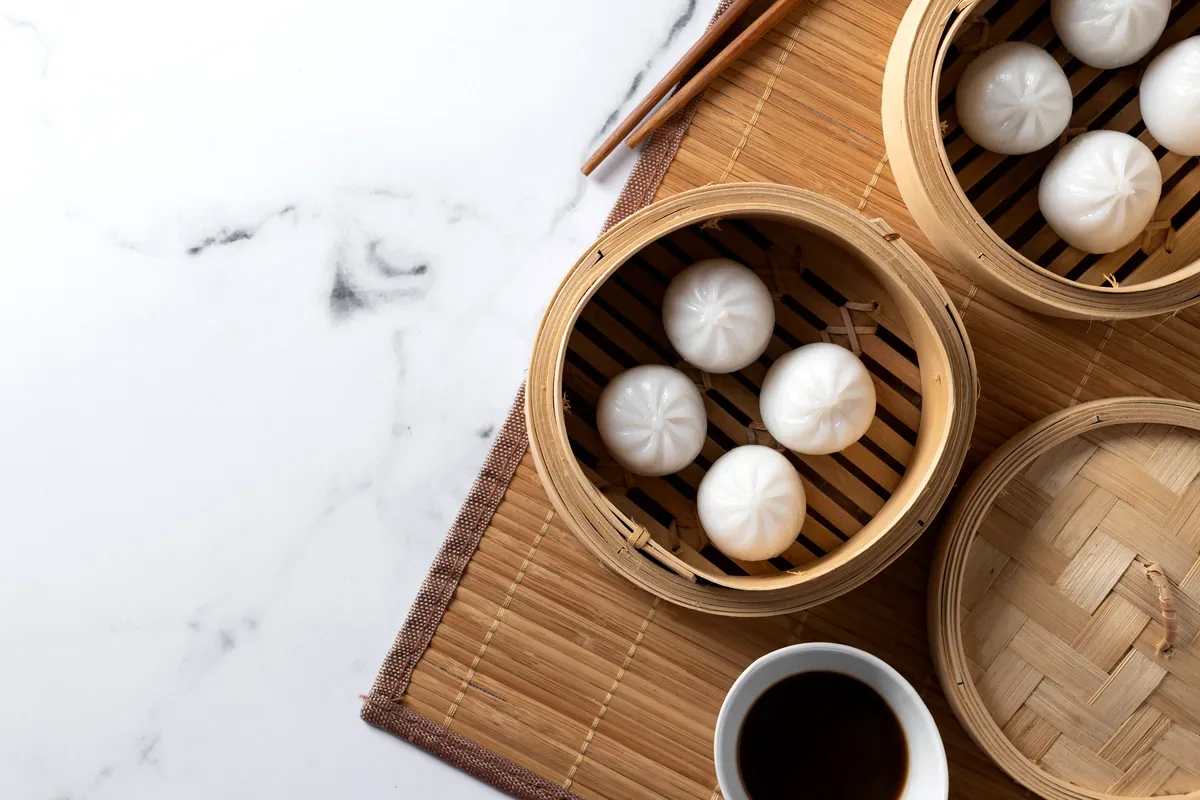 Bollos al vapor en canastas de bambú junto a una taza de té