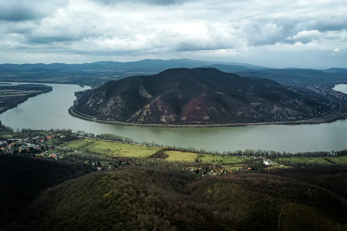 Vista aérea de un río ancho que rodea una colina, con montañas al fondo