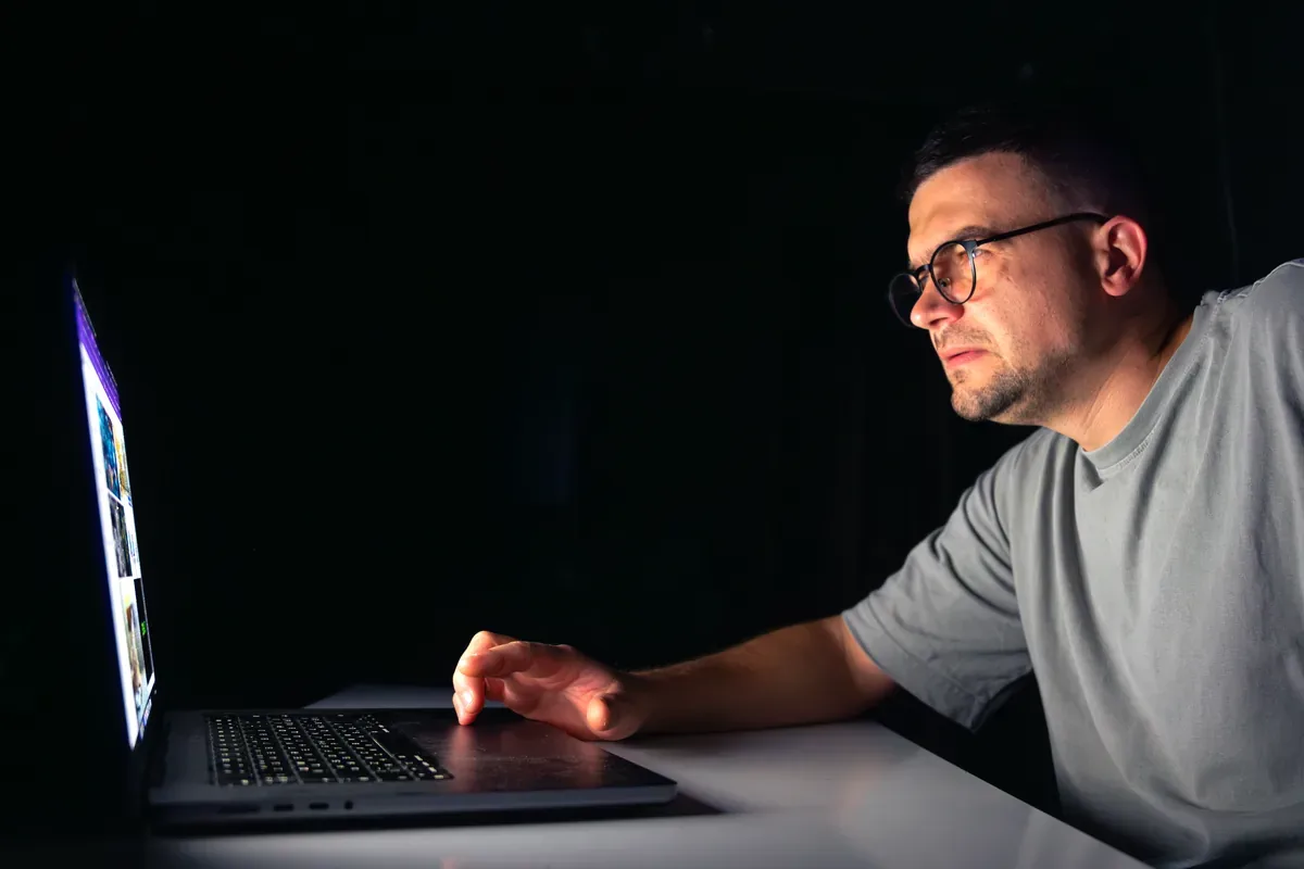 Hombre con anteojos que trabaja de noche frente a una computadora portátil