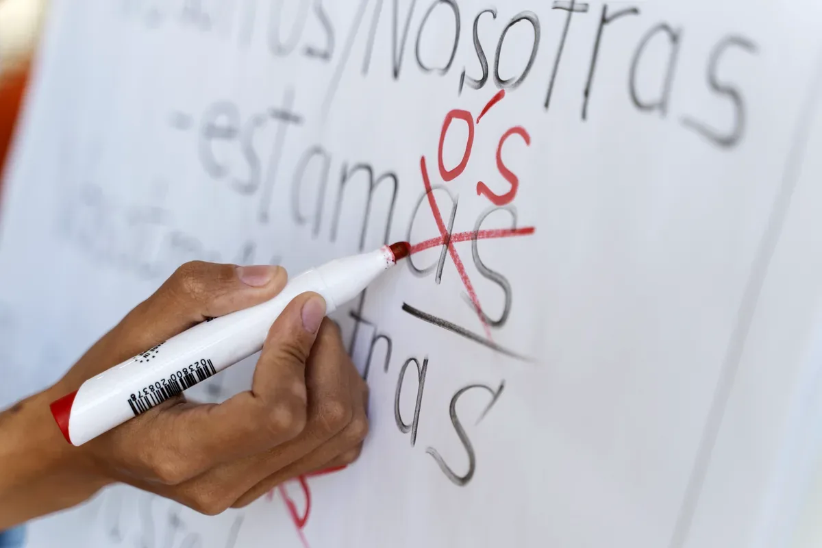 Mano que corrige con un marcador rojo palabras escritas en un pizarrón