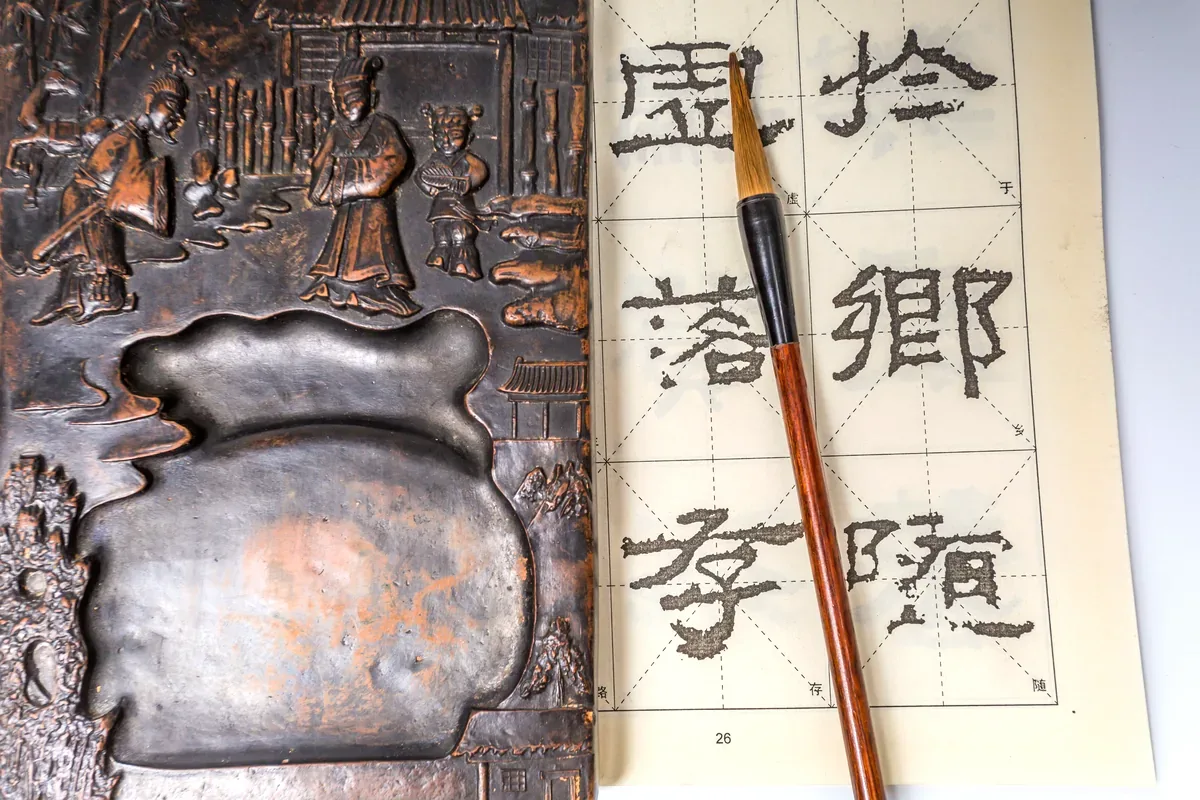 Pincel y piedra de tinta junto a una hoja con caracteres chinos
