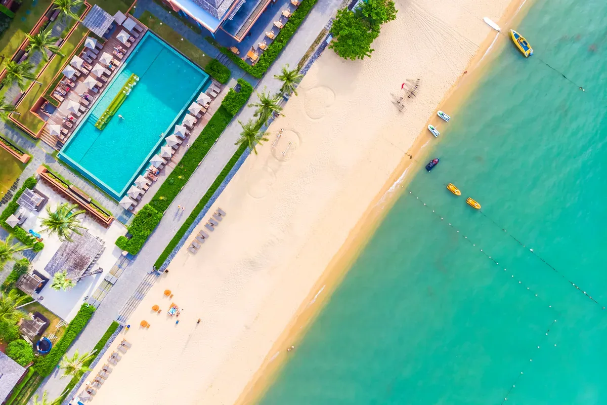 Vista aérea de un hotel con piscina frente a una playa de arena blanca