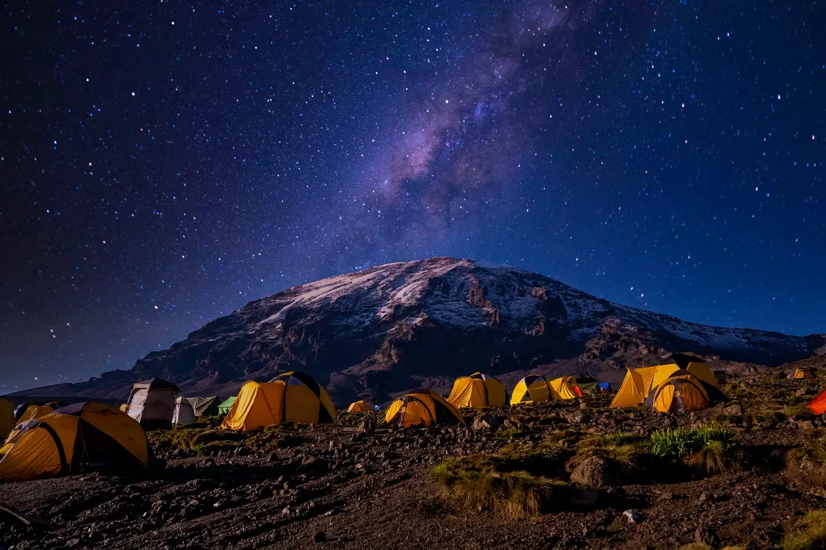 Carpas iluminadas al pie de una montaña bajo un cielo estrellado