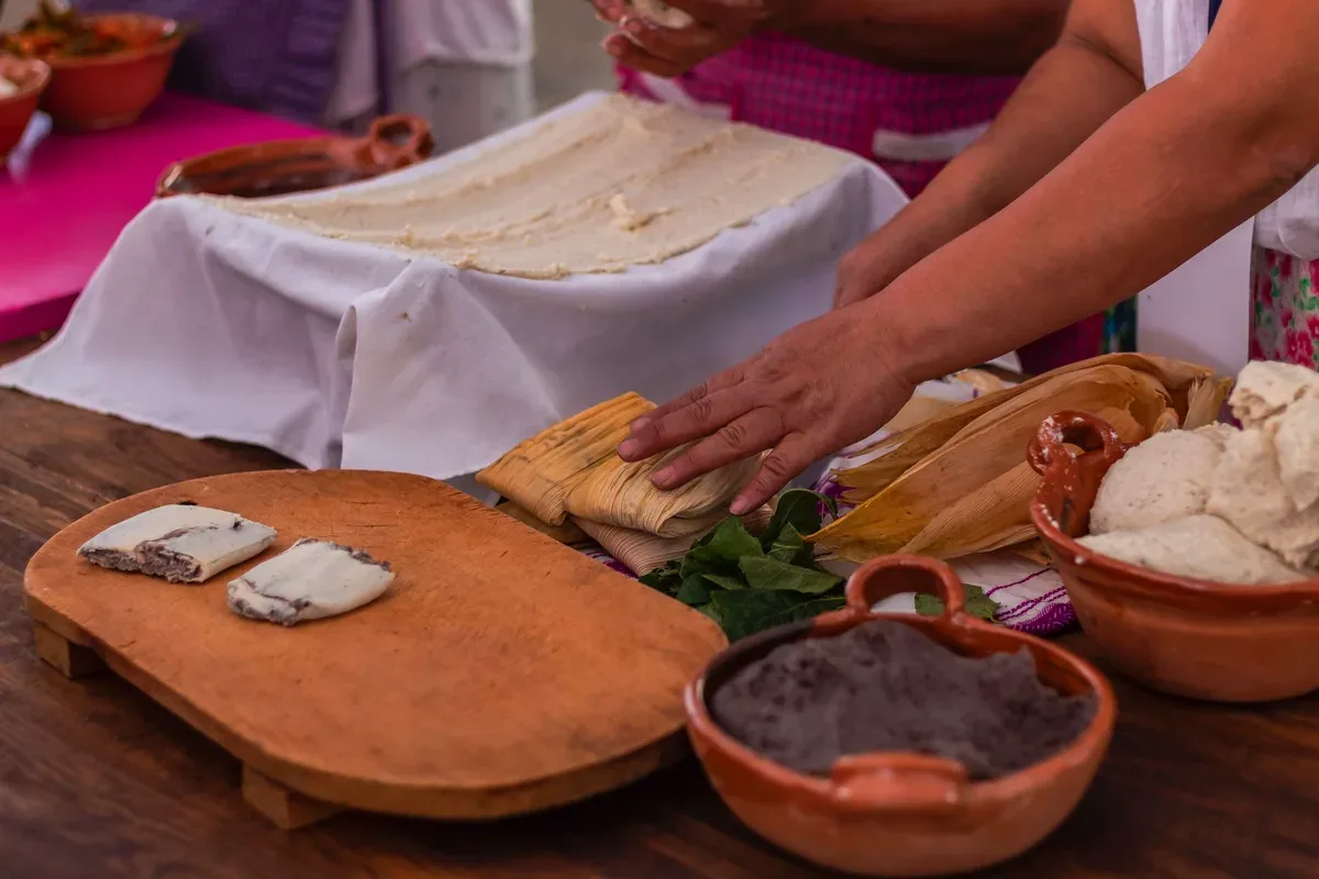 Mujeres que preparan tamales envueltos en hojas sobre una mesa de madera