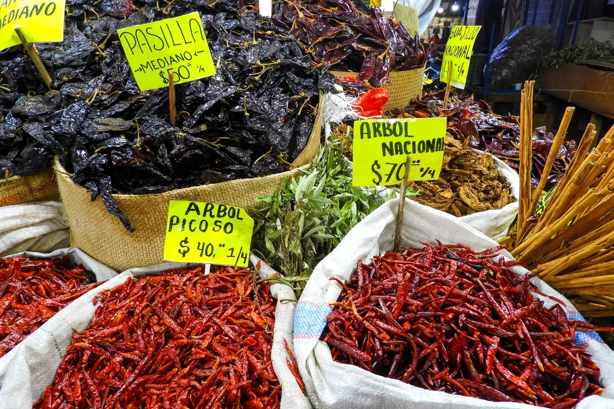 Costales de chiles secos con carteles de precio en un mercado