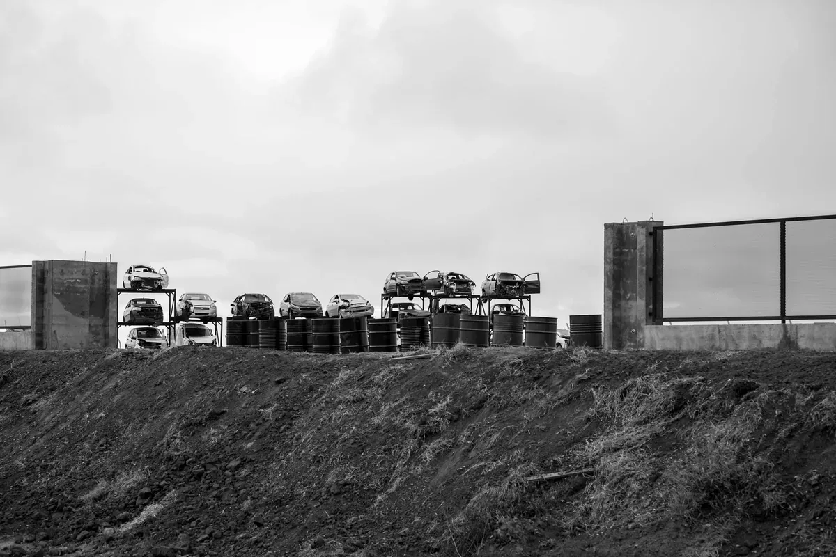 Autos apilados en un depósito detrás de un muro, en blanco y negro