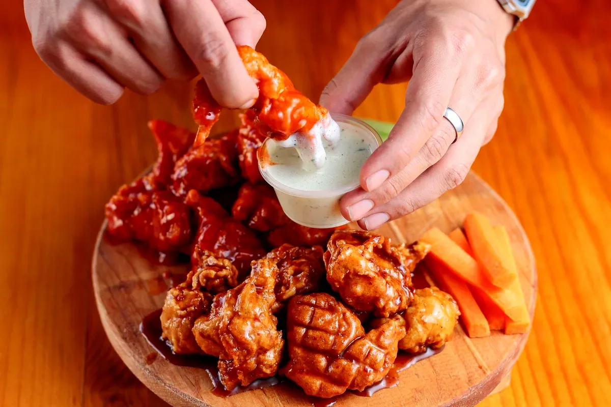 Alitas de pollo con salsa y bastones de zanahoria en una tabla de madera
