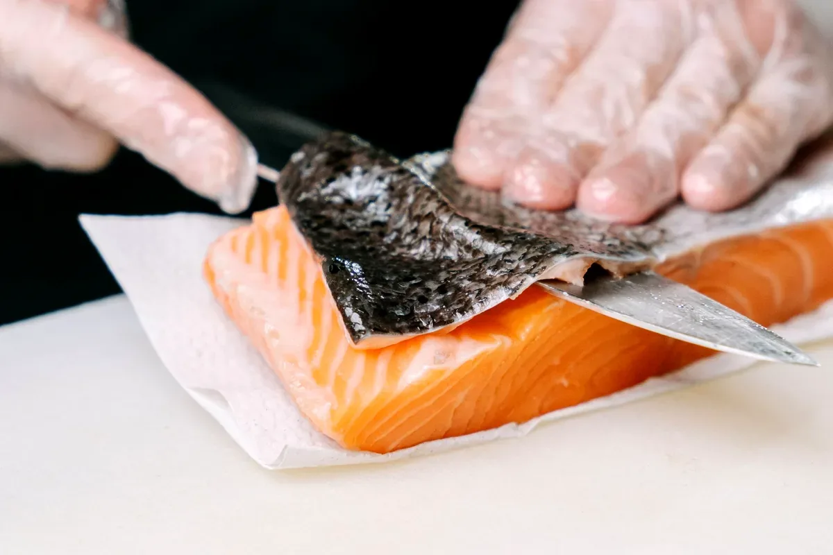Manos con guantes que quitan la piel a un filete de salmón con un cuchillo