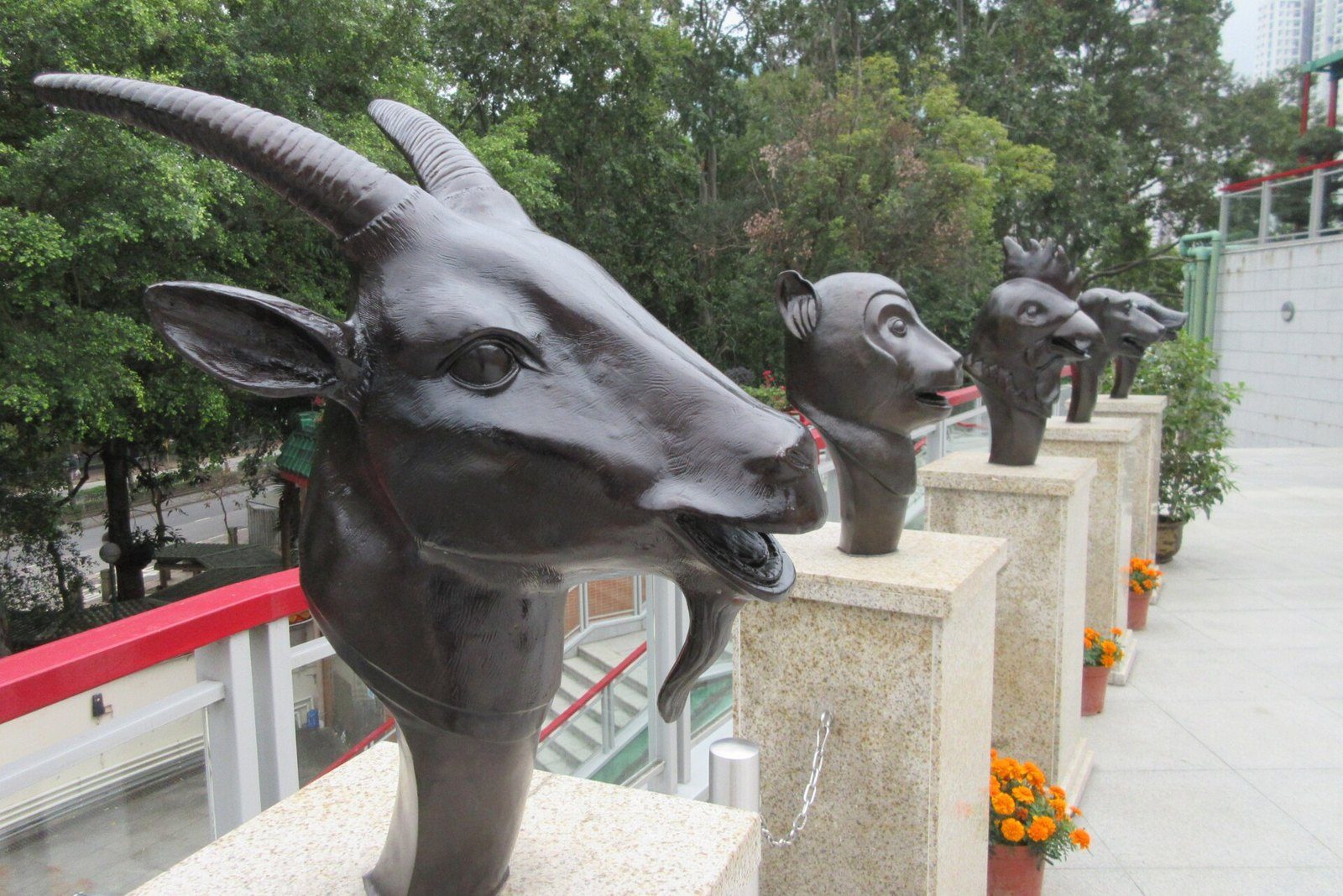 Escultura de bronce de la cabeza de una cabra con cuernos, junto a otras cabezas del zodiaco chino sobre pedestales en un templo