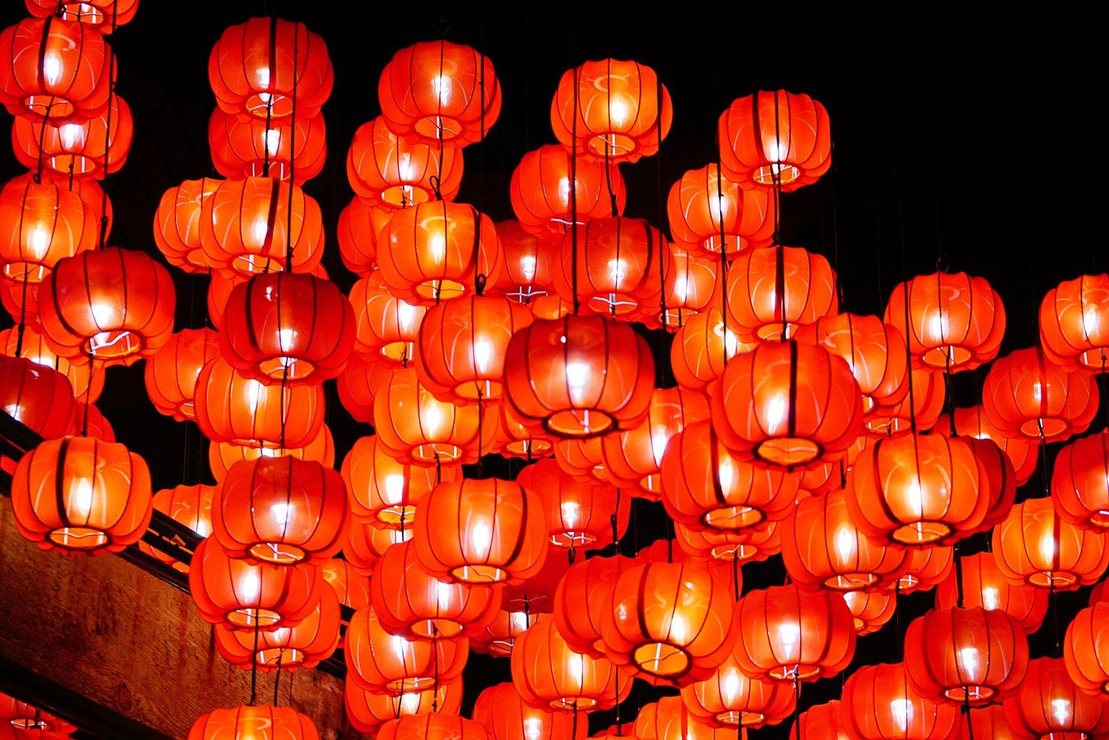 Decenas de faroles rojos encendidos colgados en la noche, formando un techo de luz anaranjada