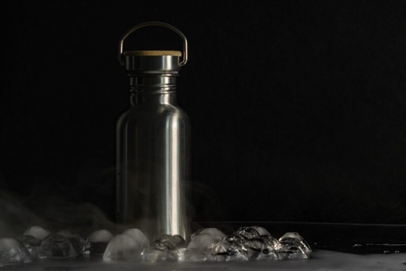 Botella de acero inoxidable con cubos de hielo sobre fondo negro
