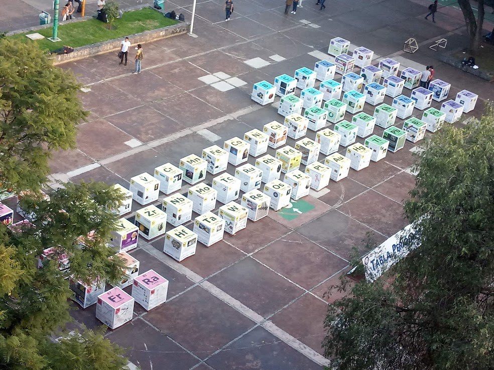 Vista desde arriba de una plaza con cubos blancos y de colores acomodados como una tabla periódica gigante en el patio de una facultad